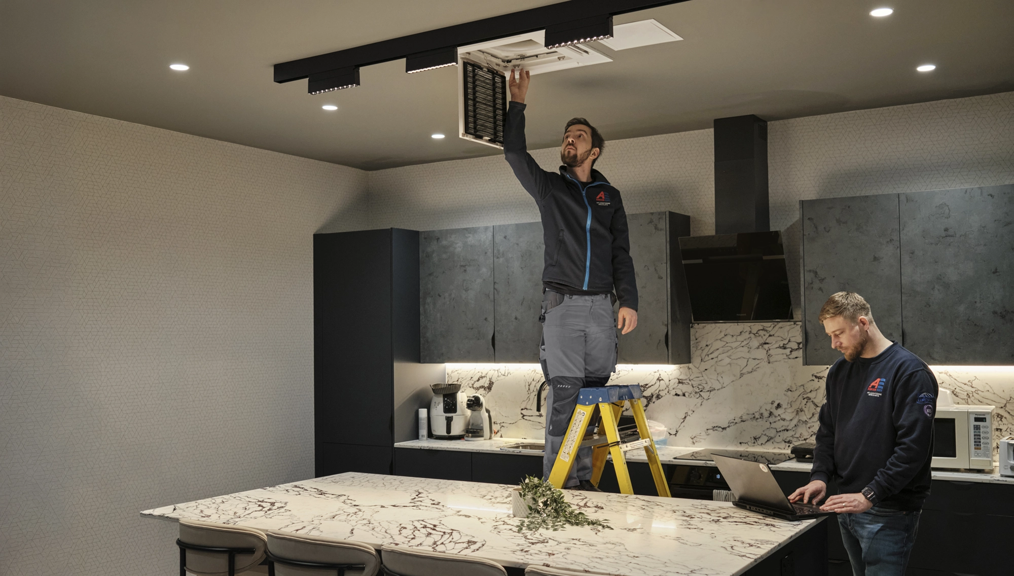 Aircon Elite engineers installing a ceiling-mounted air conditioning unit in a modern kitchen