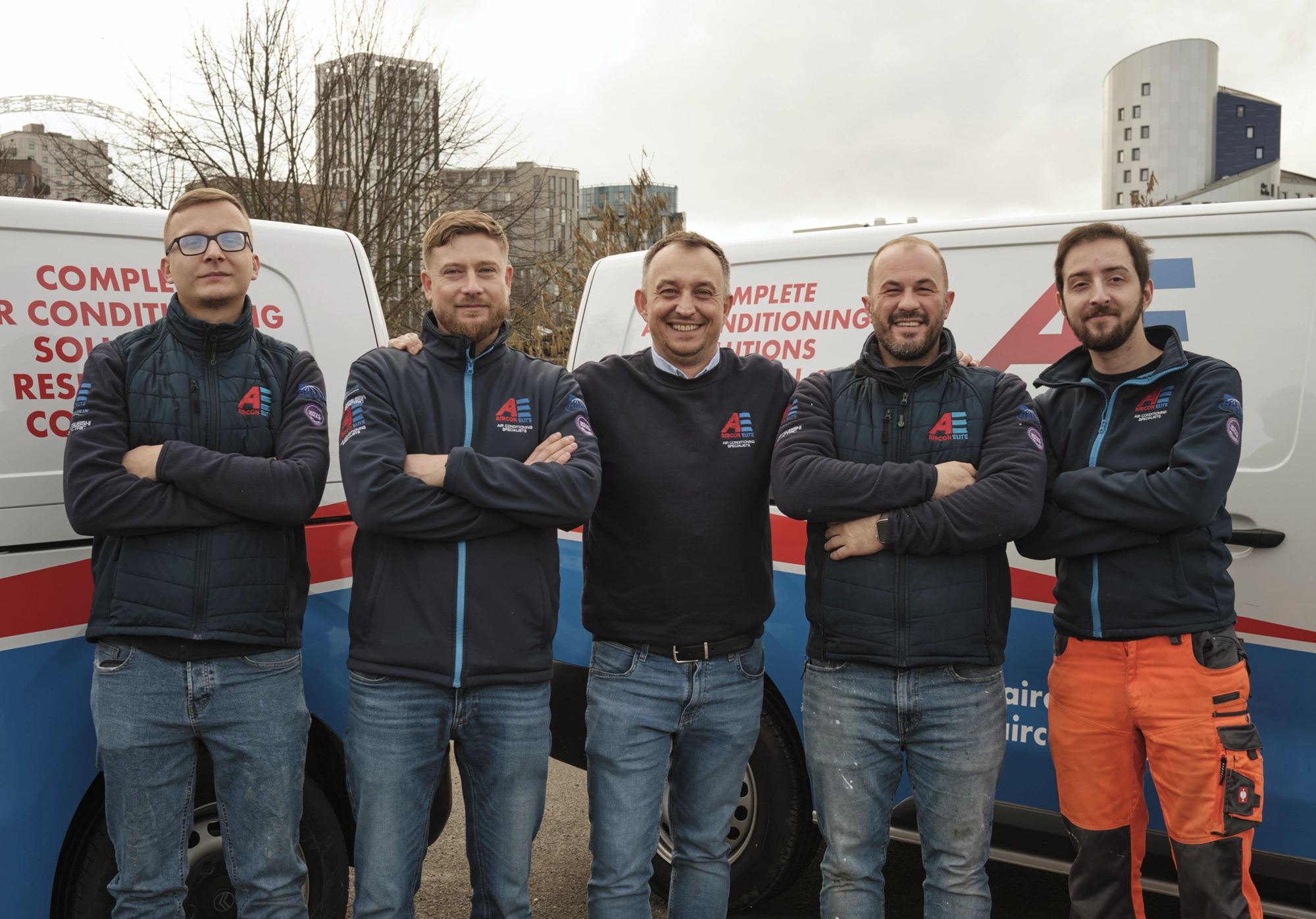 Aircon Elite team of five engineers standing together in front of service vans